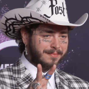 Post Malone in a cowboy hat that says "Post" doing a peace sign with his fingers