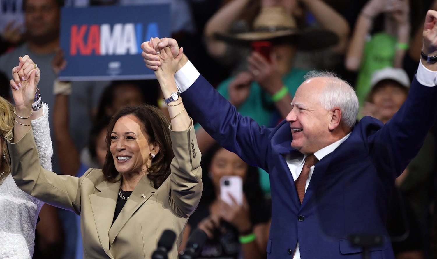 Kamala Harris and Tim Walz raising hands in front of a KAMALA sign