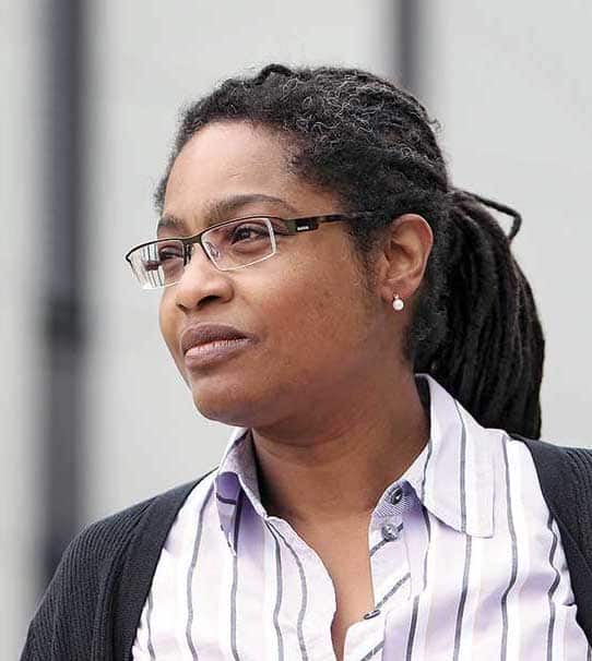Black woman, in glasses and braids in ponytail looking to the left off camera.